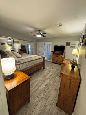Quarto com cama, mesas de cabeceira, escrivaninha, ventilador de teto e televisão.
