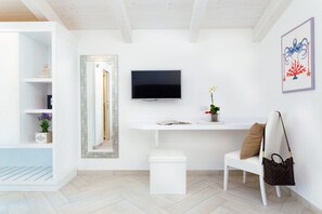 A modern, minimalist living room with a flat-screen TV, white furniture, and a small plant.