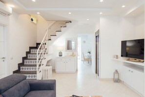 A modern living room with a grey sofa, a staircase with patterned steps, a white cabinet, and a TV on a white shelf. - MyExclusiveItaly - Spacious Villa with 4 rooms, pool, solarium&garden (Sant'Agnello)