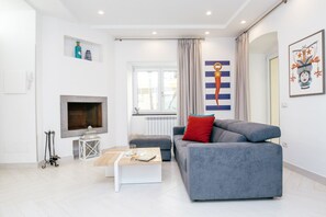 Una sala de estar moderna con un sofá gris, una mesa de centro blanca, una chimenea y un ventanal con cortinas.