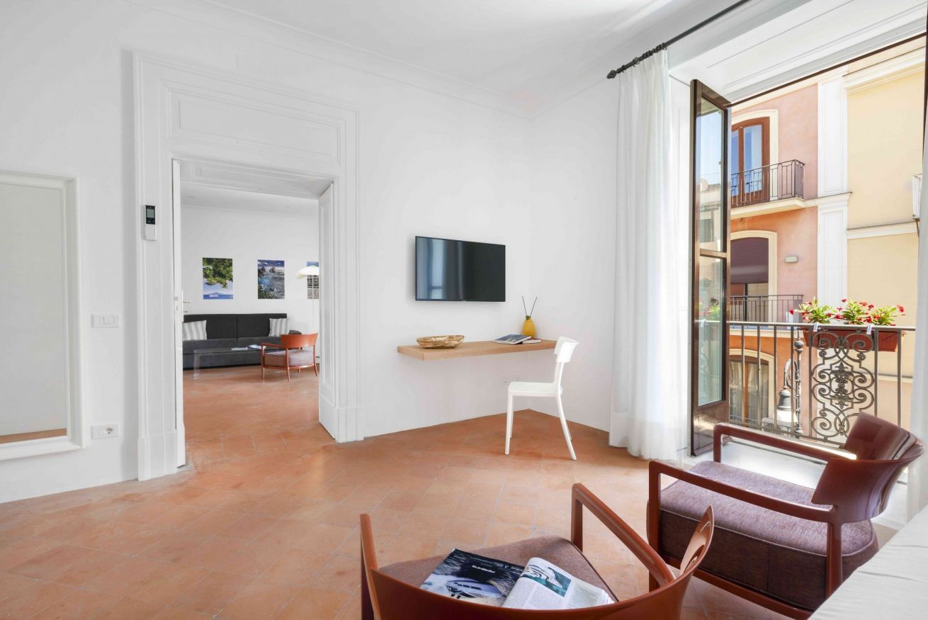 Un salon moderne doté d’un téléviseur à écran plat, d’une table à manger avec des chaises, d’un fauteuil blanc et d’un balcon avec une balustrade.