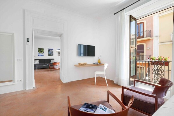 Una sala de estar moderna con un televisor de pantalla plana, una mesa de comedor con sillas, una silla blanca y un balcón con barandilla.