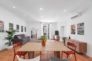 Una sala moderna con una mesa de comedor de madera, sillas rojas, un sofá gris y un televisor sobre un mueble de madera.