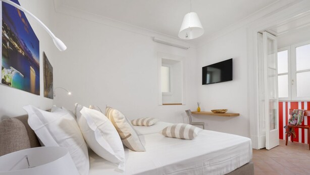 A modern bedroom with a large bed, a flat-screen TV, and a window with a view of the cityscape. - Deluxe Home in Sorrento Old Town with Balconies (Sorrento)