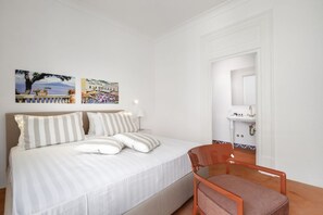 Un dormitorio con cama, una silla y dos cuadros en la pared que muestran paisajes.