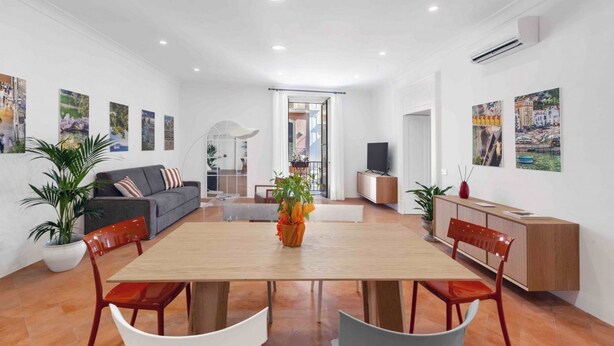 Una sala moderna con una mesa de comedor de madera, sillas rojas, un sofá gris y un televisor sobre un mueble de madera.