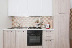 Une cuisine compacte équipée d’une cuisinière à gaz, d’un four et d’un lave-vaisselle, avec des meubles de couleur bois clair et un dosseret à carreaux.