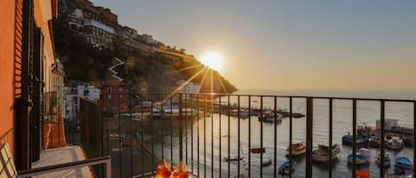A balcony with a view of a harbor at sunset, featuring boats and buildings along the coastline.