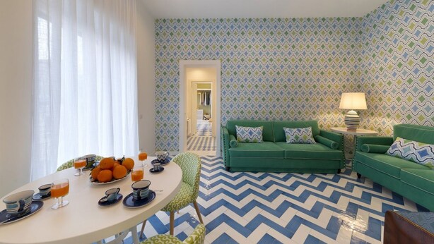 A modern living room with a green sofa set, a dining table with orange fruits, and patterned walls. - Luxury Four Bedroom Home (Sorrento)