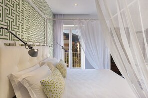A bedroom with a large bed, white bedding, a geometric patterned wall, and a view through a glass door to the outside.