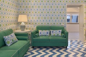 A room with a green sofa, a striped lamp, and patterned wallpaper.