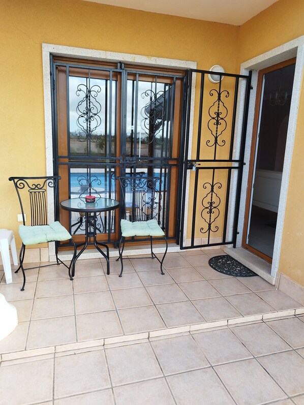 A small patio with a table and two chairs, a sliding glass door, and a yellow wall.