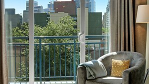 Ein Balkon mit Blick auf eine Stadtlandschaft, ein grauer Sessel mit einem gemusterten Kissen und ein Fenster mit Vorhängen.