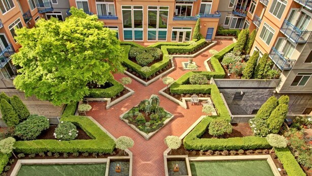 Ein Innenhof mit geometrischen Gärten, einer zentralen Fontäne und einem großen Baum.