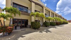 A hotel with a curved facade, multiple balconies, and a paved courtyard with palm trees and shrubs.
