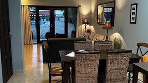 A spacious living area with a dining table, wicker chairs, a sofa, and a ceiling fan.