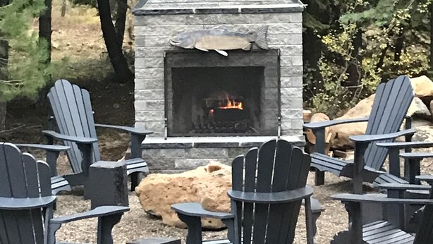 Una chimenea de piedra con fuego, rodeada de sillas Adirondack y un banco de piedra.