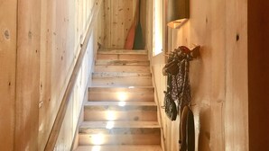 Una escalera de madera con una lámpara fijada a la pared y un perchero colgado.