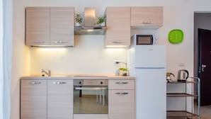 A modern kitchen with light wood cabinets, a built-in oven, a microwave, and a stainless steel refrigerator.