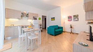 A modern kitchen with white cabinets, a dining area with a table and chairs, and a teal sofa in a living area.