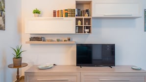 A modern living room with a flat-screen TV, wooden cabinets, a bookshelf, and a potted plant.