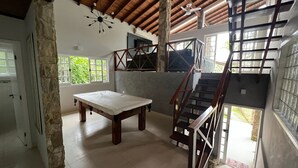 Una habitación espaciosa con techo alto, una escalera de madera, un ventanal grande y una mesa.