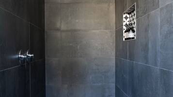 Shower area features a geometric patterned floor, dark tile enclosure, and a showerhead mounted on the ceiling.