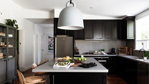 A modern kitchen with dark cabinets, a central island with a white countertop, and a hanging light fixture. - Fingal House-Ultimate Escape for Groups, Families & Retreats (Fingal)
