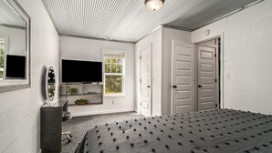 Un dormitorio con una cama grande, televisión, cómoda, espejo y ventana.