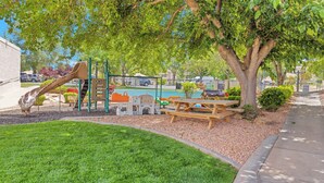 A playground with a slide and climbing structures, surrounded by trees and a picnic table. - Villas at Southgate (St. George)