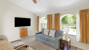 A living room with a flat-screen TV, a sofa, a coffee table, and a ceiling fan. - Villas at Southgate (St. George)