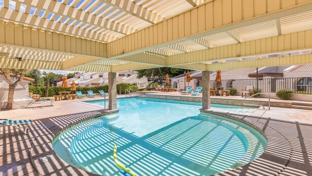 A pool area with a covered deck, lounge chairs, and umbrellas. - Villas at Southgate (St. George)