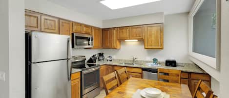 A compact kitchen with wooden cabinets, stainless steel appliances, and a dining table with chairs.
