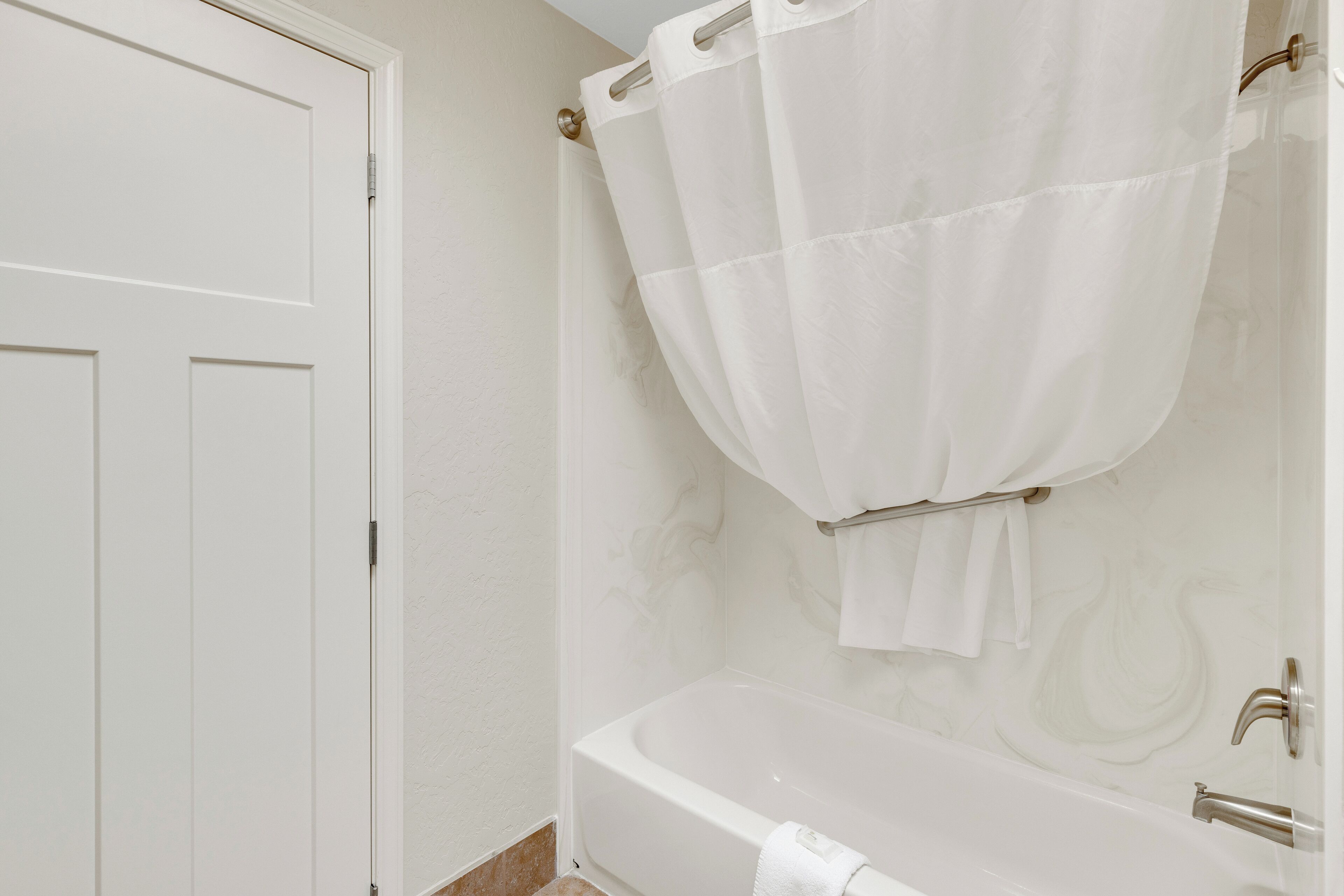 Un bagno con una vasca da bagno bianca, una porta bianca e una tenda da doccia.