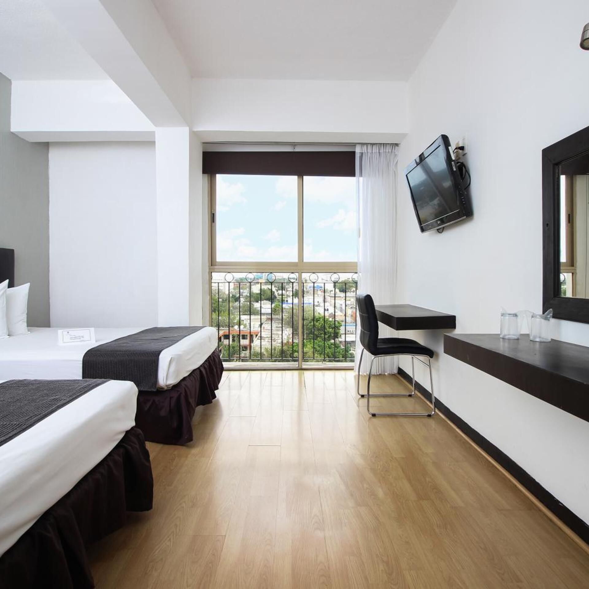 Une chambre d’hôtel avec deux lits, un bureau, une chaise, une télévision et un balcon donnant sur la ville.