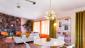 A modern living room with a round white table, orange chairs, a white sofa, and a stone wall.
