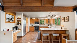 A spacious kitchen with wooden cabinets, a central island with stools, a stainless steel refrigerator, and a hanging light fixture. - Spacious Luxury Home Close to Downtown and Ski, Private Hot Tub, Amazing Views (Durango)