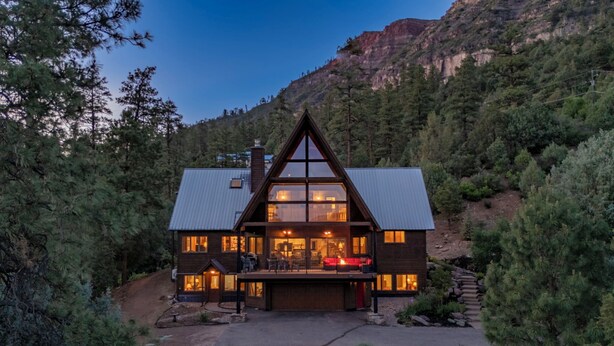 A cabin with a large deck, surrounded by trees and a mountain backdrop. - Spacious Luxury Home Close to Downtown and Ski, Private Hot Tub, Amazing Views (Durango)