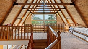 A high-ceilinged attic bedroom with a wooden beam structure, a window overlooking a mountain, and a bunk bed. - Spacious Luxury Home Close to Downtown and Ski, Private Hot Tub, Amazing Views (Durango)