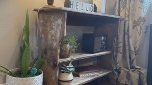 A wooden console table with a 'HELLO' sign, a lamp, a radio, and shelves with decorative items and plants.