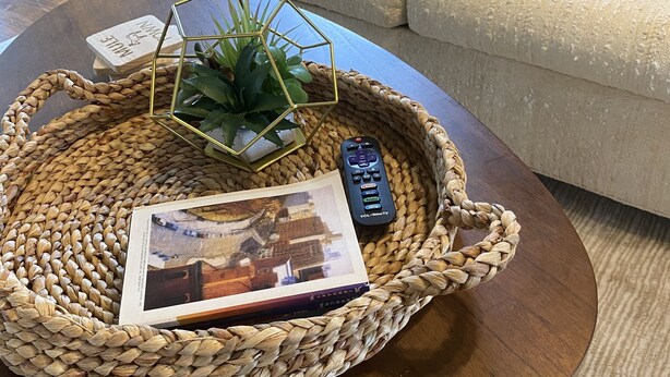A woven tray on a round coffee table with a remote control, a magazine, and a small plant.