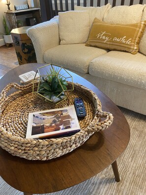 A woven tray on a round coffee table with a remote control, a magazine, and a small plant.