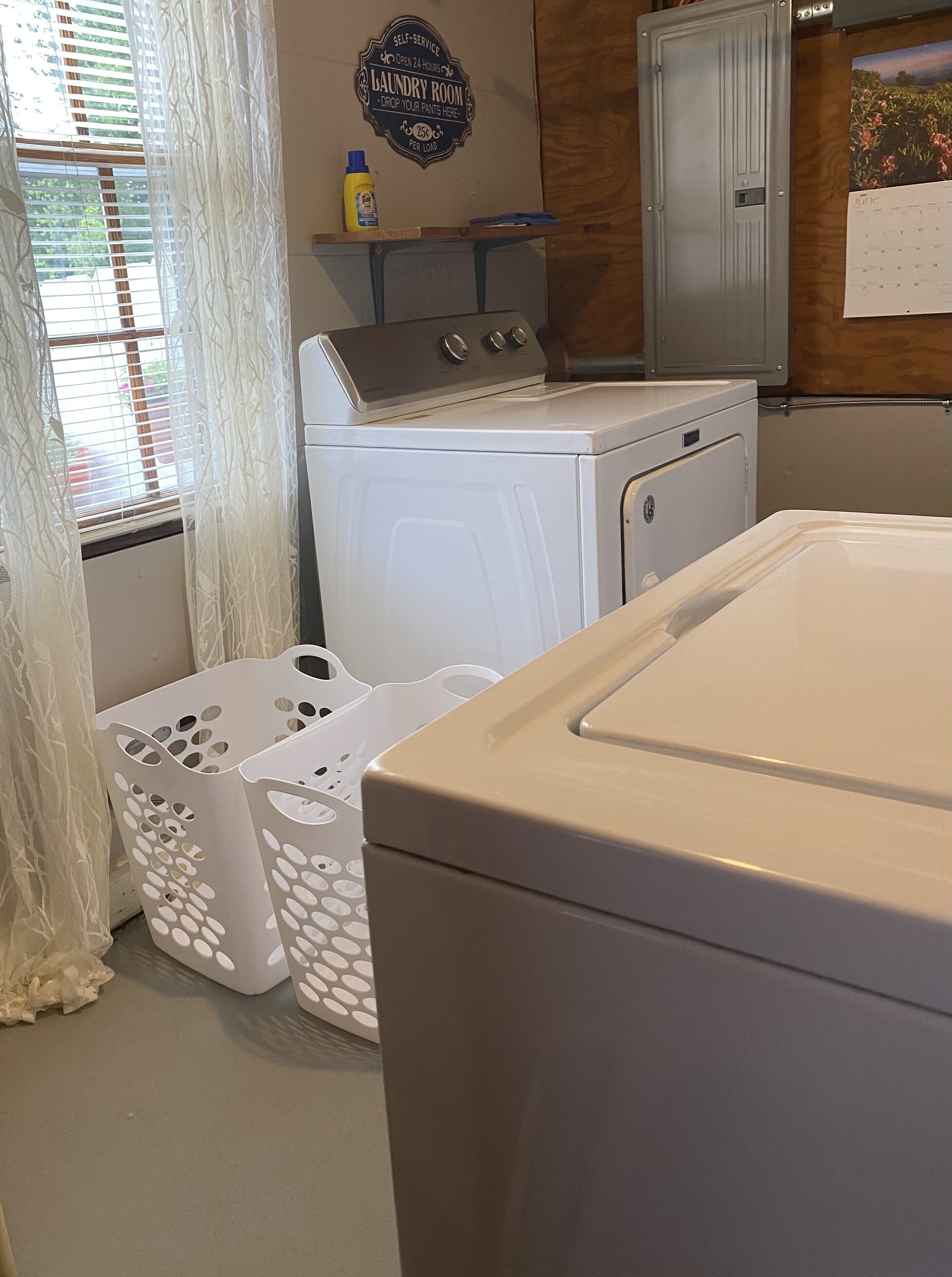 A laundry room with a washer and dryer, a self-service laundry sign, and a calendar on the wall.