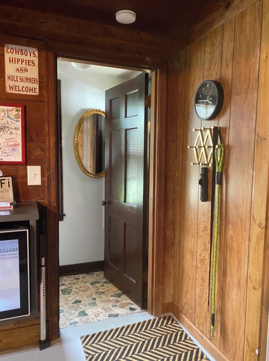 Un interior de madera con puerta, espejo, reloj y perchero en la pared.