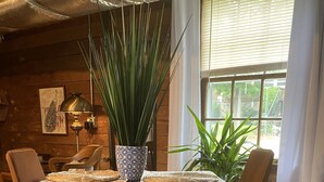 A dining area with a round table, chairs, a woven rug, and potted plants.