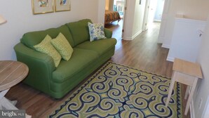 A green sofa with patterned cushions, a patterned rug, and two framed artworks on the wall. - Gorgeous 3 Bedroom Townhouse, Bethany Beach, steps from pool and fitness center (Bethany Beach)