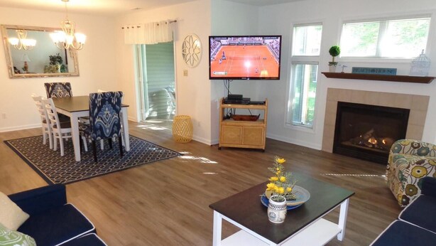 A living room with a TV, fireplace, and a dining area with chairs and a table. - Gorgeous 3 Bedroom Townhouse, Bethany Beach, steps from pool and fitness center (Bethany Beach)