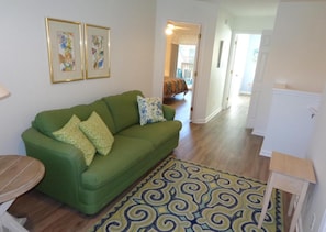 Un canapé vert agrémenté de coussins à motifs, un tapis à motifs et deux œuvres d’art encadrées accrochées au mur.