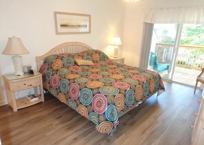 Une chambre avec un lit en bois, deux tables de chevet avec des lampes, un tableau encadré au mur et une vue sur l’extérieur par une porte-fenêtre coulissante.