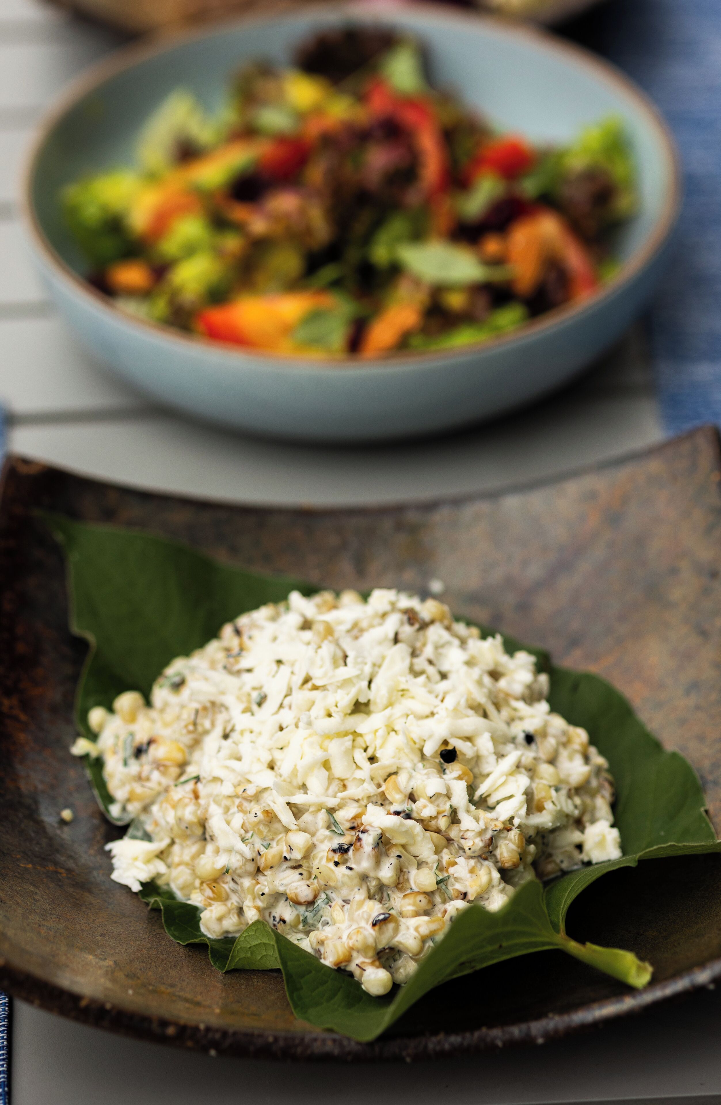A bowl of rice on a leaf with a salad in the background.